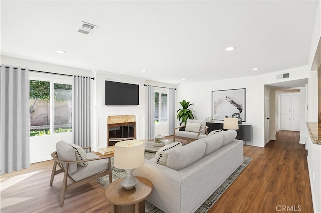 living area with a premium fireplace, visible vents, dark wood-style flooring, and recessed lighting