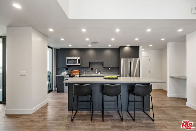 kitchen with sink, gray cabinetry, stainless steel appliances, a center island, and a kitchen bar