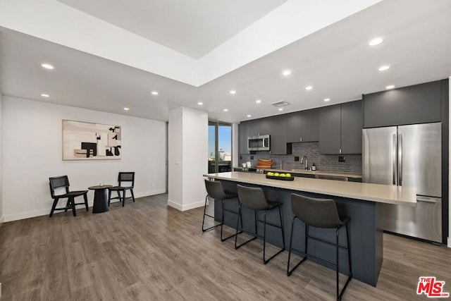 kitchen with appliances with stainless steel finishes, a breakfast bar, wood-type flooring, sink, and backsplash