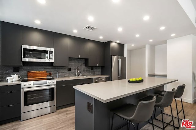 kitchen with appliances with stainless steel finishes, sink, a kitchen breakfast bar, a center island, and light hardwood / wood-style flooring