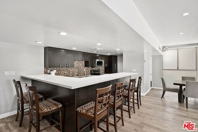 kitchen featuring a breakfast bar area, appliances with stainless steel finishes, backsplash, kitchen peninsula, and light wood-type flooring