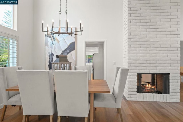 dining room with a brick fireplace, hardwood / wood-style flooring, a notable chandelier, and a high ceiling