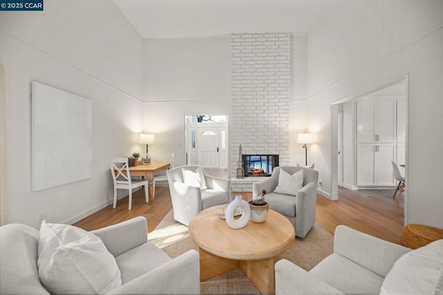 living room with a towering ceiling, a brick fireplace, and light hardwood / wood-style flooring