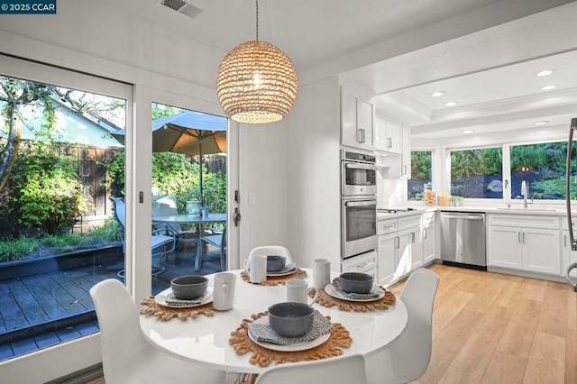 kitchen featuring sink, appliances with stainless steel finishes, white cabinetry, hanging light fixtures, and light hardwood / wood-style floors