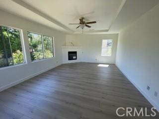 unfurnished living room featuring dark wood-type flooring, plenty of natural light, a raised ceiling, and ceiling fan