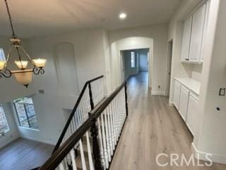 hallway with an inviting chandelier and light wood-type flooring