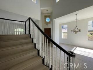 staircase with a towering ceiling, hardwood / wood-style floors, and a notable chandelier