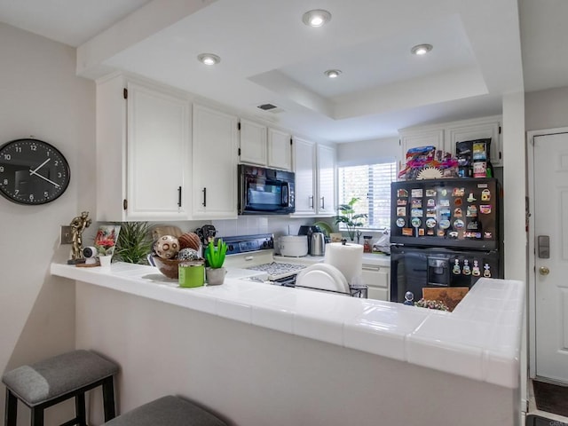 kitchen featuring white cabinetry, tile counters, black appliances, a raised ceiling, and kitchen peninsula