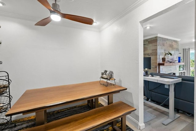 dining room with ceiling fan, ornamental molding, a stone fireplace, and light wood-type flooring