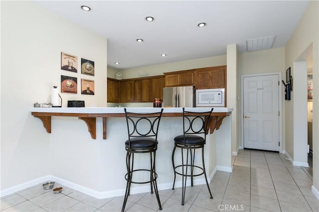 kitchen with white microwave, a breakfast bar area, stainless steel fridge, light tile patterned floors, and kitchen peninsula