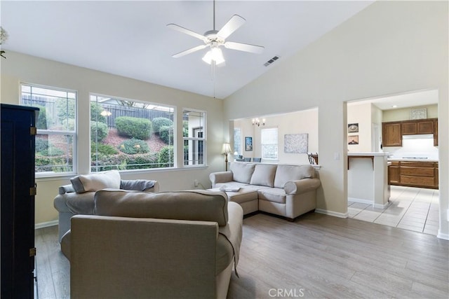 living room featuring high vaulted ceiling, ceiling fan with notable chandelier, and light hardwood / wood-style flooring