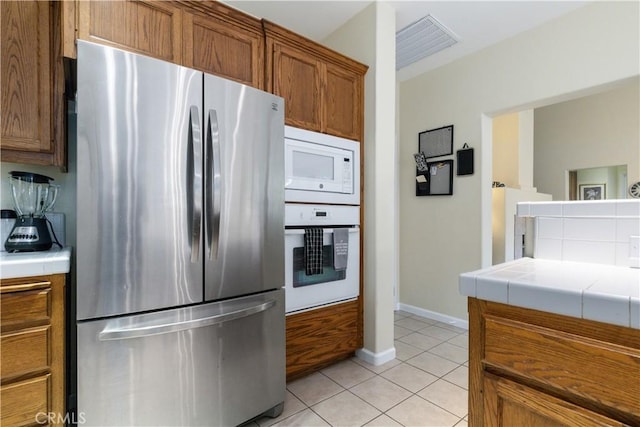 kitchen featuring light tile patterned floors, white appliances, tile counters, and decorative backsplash