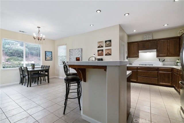 kitchen featuring cooktop, a center island with sink, a kitchen breakfast bar, and light tile patterned floors