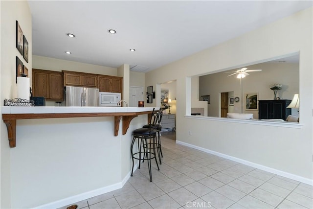 kitchen with light tile patterned floors, stainless steel fridge, a kitchen breakfast bar, kitchen peninsula, and white microwave