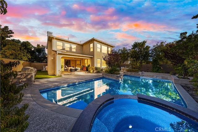 pool at dusk with a patio area and an in ground hot tub