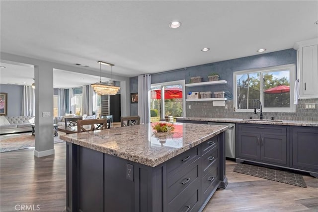 kitchen featuring a sink, light stone counters, a kitchen island, stainless steel dishwasher, and wood finished floors