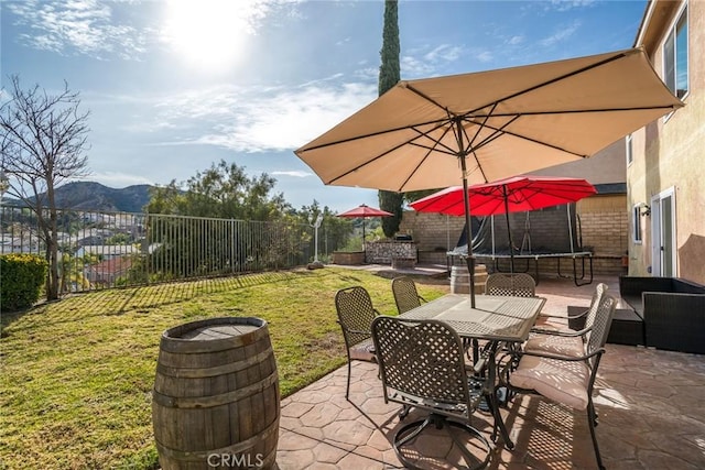 view of patio / terrace with outdoor dining space, a trampoline, a fenced backyard, and a mountain view