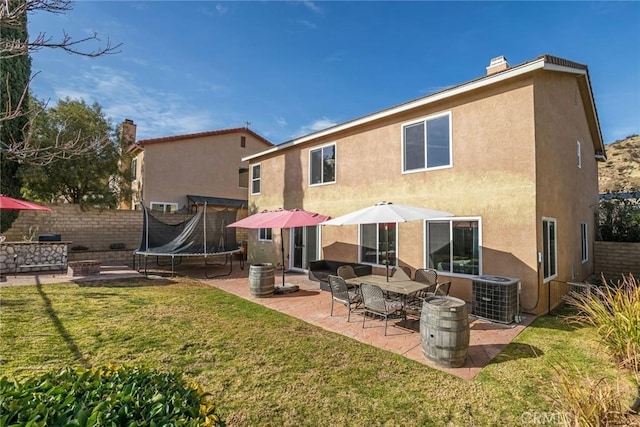 back of house featuring a yard, stucco siding, a trampoline, and fence