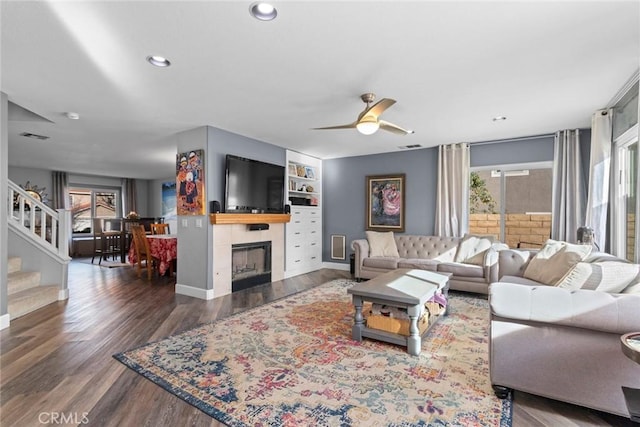 living area featuring plenty of natural light, wood finished floors, stairs, and a tiled fireplace