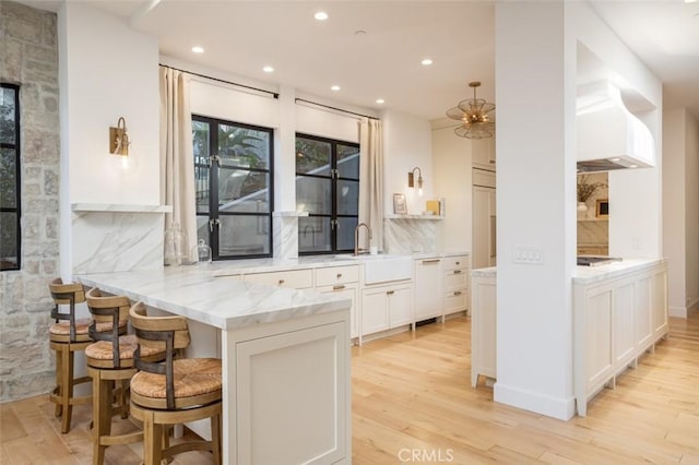 kitchen featuring white cabinetry, sink, a breakfast bar area, light stone counters, and kitchen peninsula