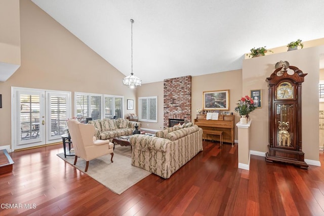 living room with a brick fireplace, dark wood-type flooring, high vaulted ceiling, and a chandelier