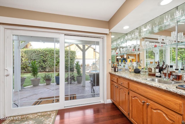 bar featuring light stone counters, sink, and dark hardwood / wood-style floors