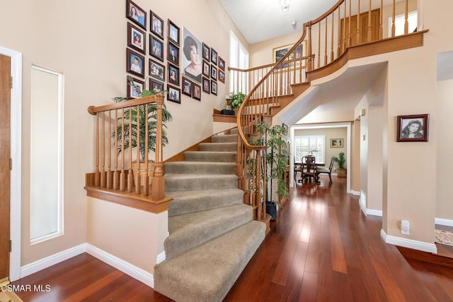 staircase with a towering ceiling and wood-type flooring