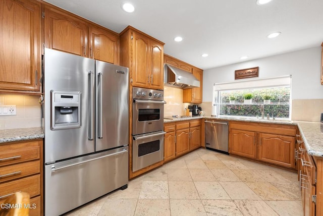 kitchen featuring appliances with stainless steel finishes, tasteful backsplash, sink, light stone counters, and wall chimney exhaust hood