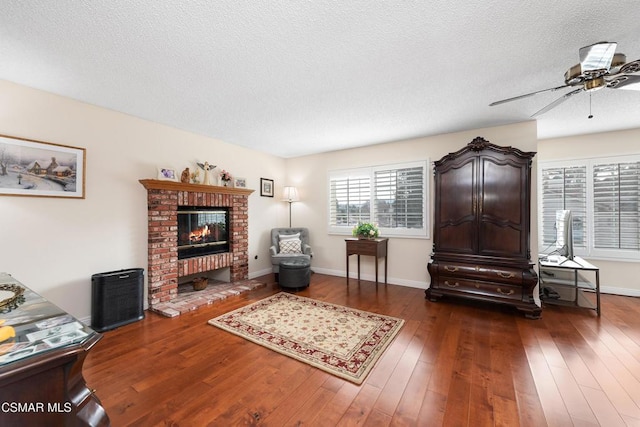 living room with ceiling fan, dark hardwood / wood-style floors, a textured ceiling, and a fireplace