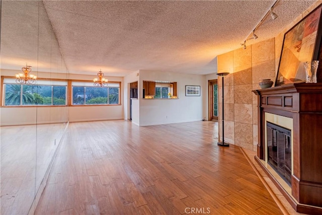 unfurnished living room featuring an inviting chandelier, hardwood / wood-style floors, a fireplace, and a textured ceiling