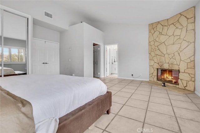 tiled bedroom with ensuite bathroom, lofted ceiling, two closets, and a fireplace