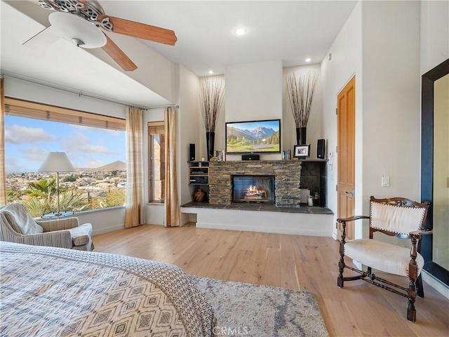 bedroom with ceiling fan, a stone fireplace, and light wood-type flooring