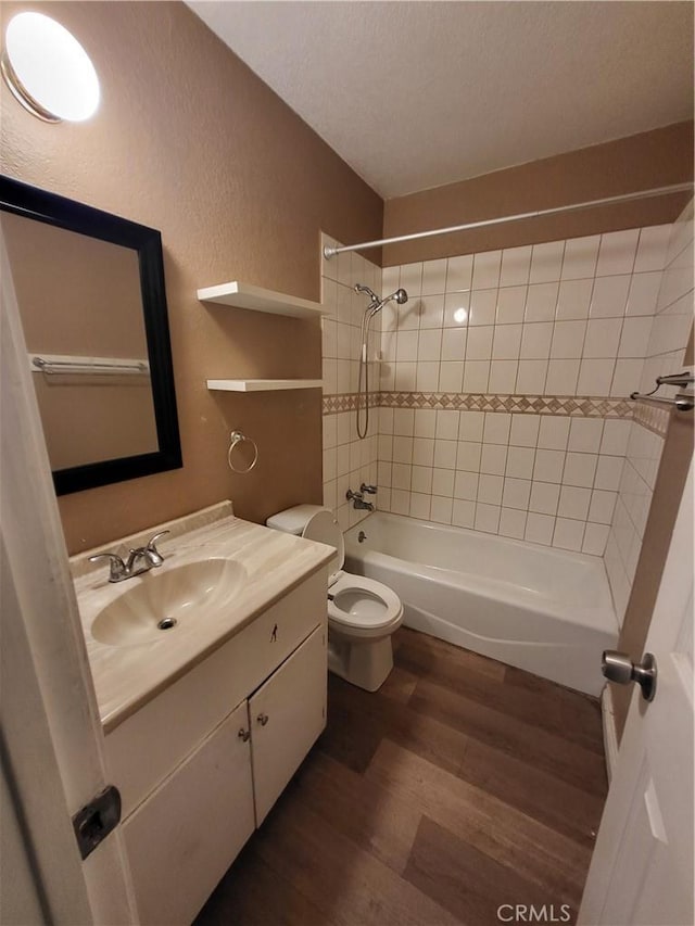 full bathroom with toilet, wood-type flooring, a textured ceiling, vanity, and tiled shower / bath combo