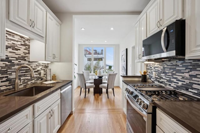 kitchen with sink, white cabinetry, stainless steel appliances, light hardwood / wood-style floors, and decorative backsplash