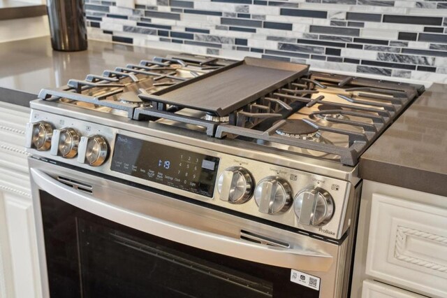 interior details with white cabinetry, stainless steel gas range oven, and backsplash