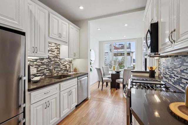 kitchen featuring sink, light hardwood / wood-style flooring, white cabinetry, stainless steel appliances, and decorative backsplash