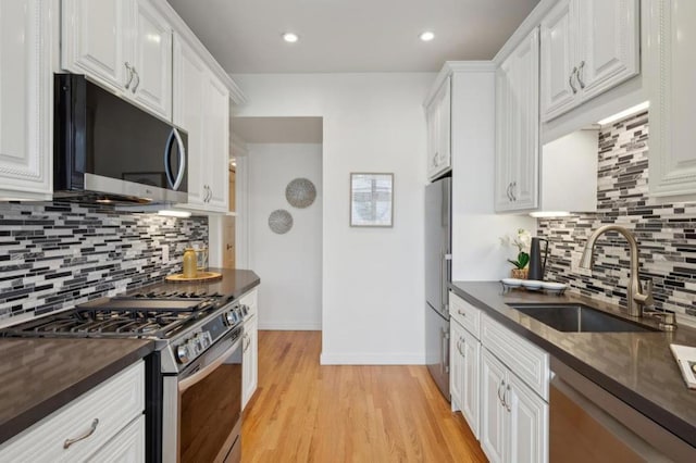 kitchen with sink, white cabinetry, light hardwood / wood-style flooring, appliances with stainless steel finishes, and backsplash