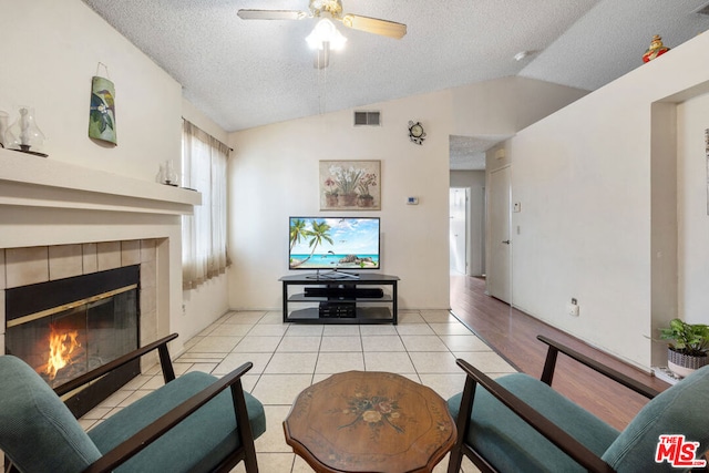 tiled living room featuring ceiling fan, a fireplace, a textured ceiling, and vaulted ceiling