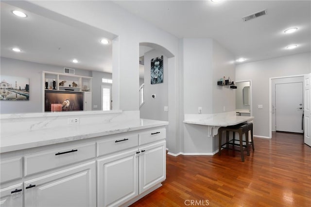 kitchen with dark wood-type flooring, light stone countertops, a kitchen breakfast bar, and white cabinets