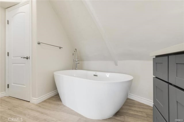 bathroom with a tub to relax in, vaulted ceiling, and wood-type flooring