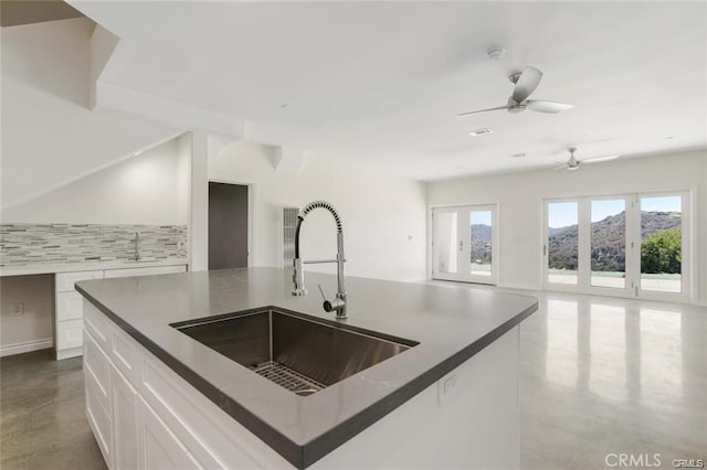 kitchen featuring sink, dark stone countertops, an island with sink, decorative backsplash, and white cabinets