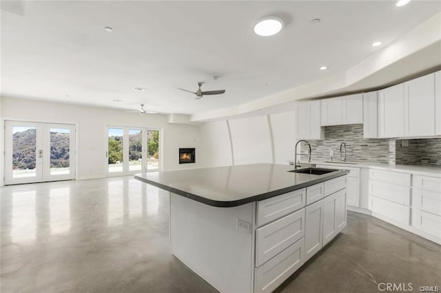 kitchen featuring tasteful backsplash, an island with sink, sink, white cabinets, and french doors