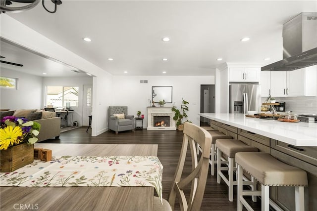 kitchen featuring a breakfast bar, island range hood, white cabinetry, stainless steel refrigerator with ice dispenser, and light stone countertops