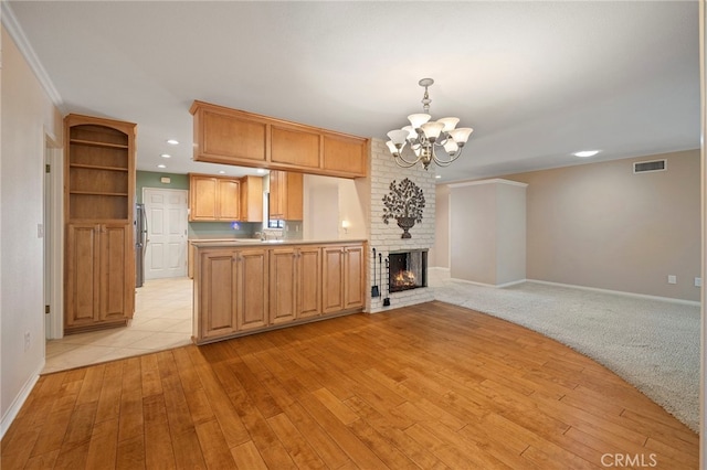 kitchen with an inviting chandelier, hanging light fixtures, a fireplace, kitchen peninsula, and light wood-type flooring