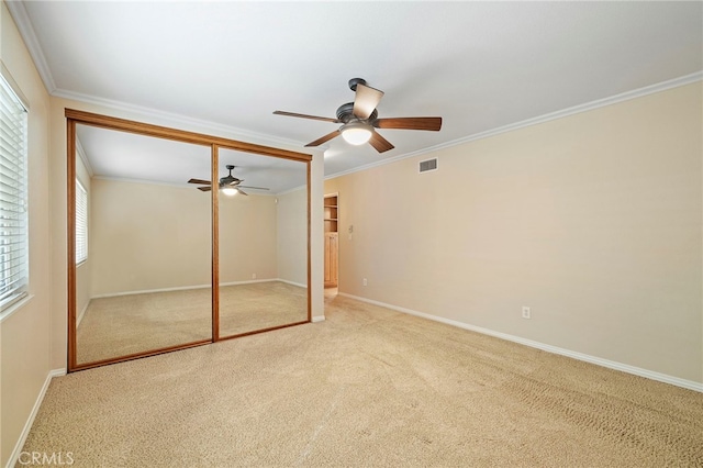 unfurnished bedroom featuring crown molding, light carpet, ceiling fan, and a closet