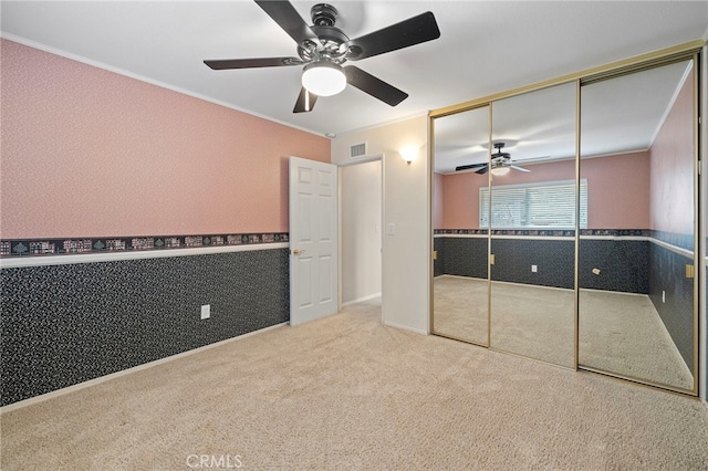 unfurnished bedroom featuring crown molding, carpet, ceiling fan, and a closet