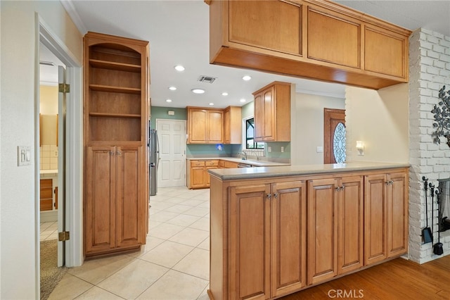 kitchen with sink, crown molding, light tile patterned floors, stainless steel refrigerator, and kitchen peninsula