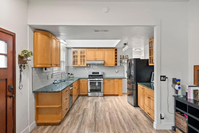 kitchen with sink, light hardwood / wood-style flooring, dark stone countertops, stainless steel appliances, and backsplash