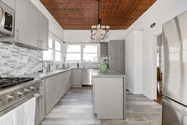 kitchen featuring a center island, gray cabinets, pendant lighting, stainless steel appliances, and decorative backsplash