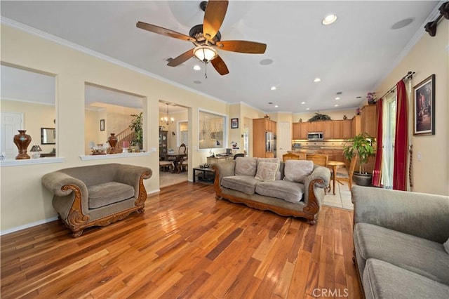 living room with crown molding, ceiling fan with notable chandelier, and light hardwood / wood-style floors